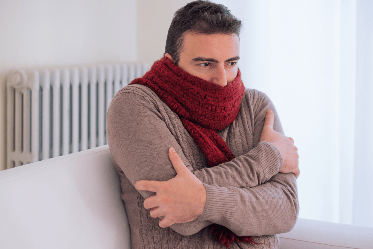 man sitting on couch wearing scarf freezing indoors