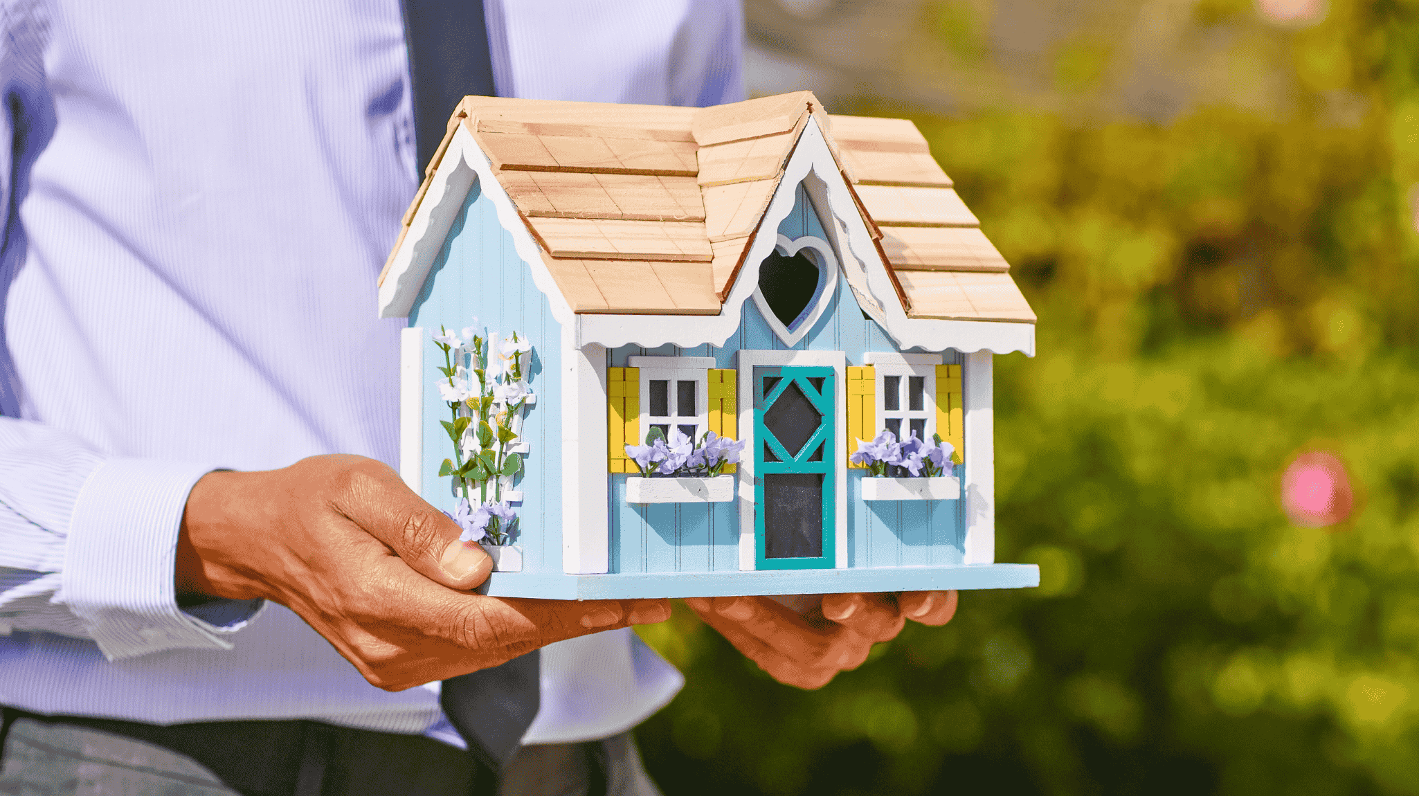 person holding wooden mini house with spring decor